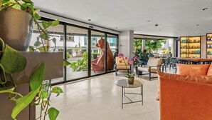 Un espacio interior amplio con un gran ventanal, una mesa redonda y una zona de estar con cojines anaranjados.