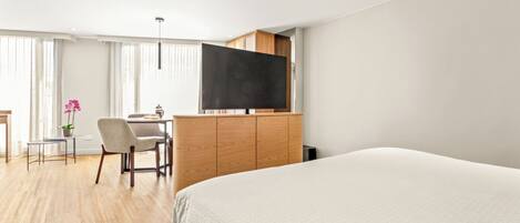 A modern hotel room with a large bed, a desk with a chair, a flat-screen TV, and a potted plant.