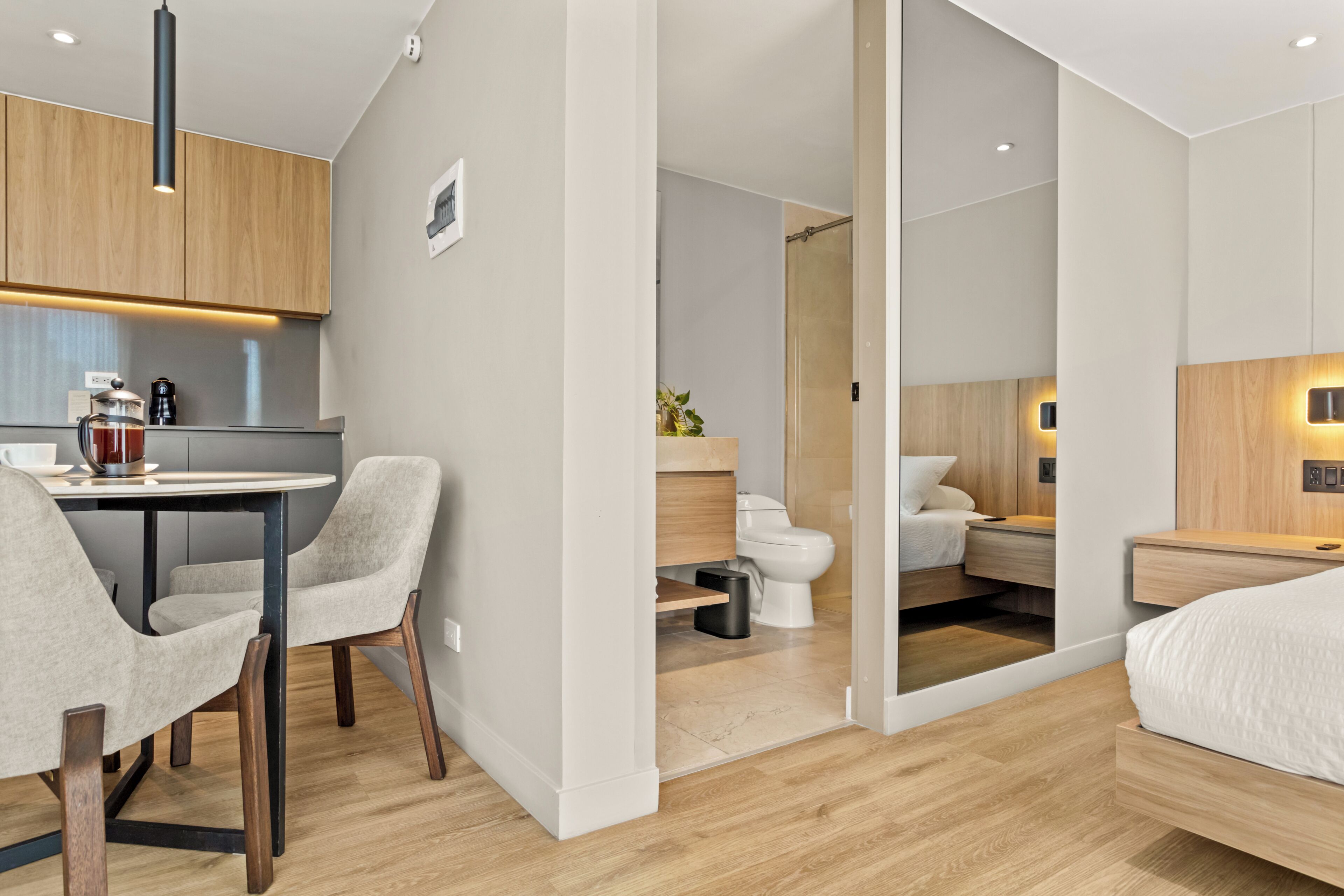 A modern hotel room with a kitchenette, a separate bathroom, and a bed.