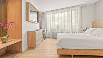 A modern bedroom with a wooden bed, a desk, and a chair, and a large window with sheer curtains.