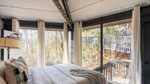 Ein Schlafzimmer mit einem großen Bett, einem Fenster mit Vorhängen und Blick ins Freie.