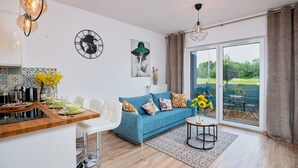 A modern living room with a blue sofa, a dining area with a kitchen counter, and large windows offering a view of the outdoors. - Poznań Grunwald - Parking & Terrace - by Rentujemy (Poznan)