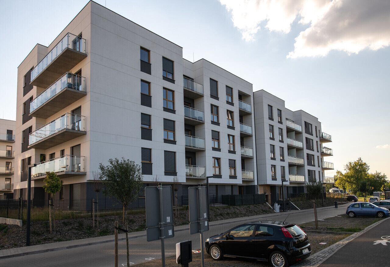 Un edificio residencial de varios pisos con balcones, un estacionamiento y vista a la calle.