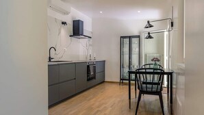 A modern kitchen with grey cabinets, a black countertop, and a dining area with a black chair and table. - Domus Beato Angelico |  two minutes from the Pantheon and Piazza della Minerva (Roma)