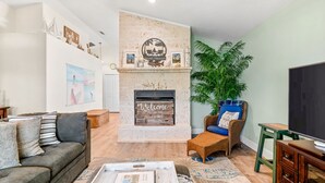 A living room with a fireplace, a sofa, a chair, a coffee table, and a television. - Heated Pool, Spa & Tiki Bar! Full Garage Game Room and Steps Away From The Beach (St. Augustine)