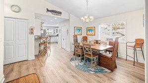 A spacious dining area with a wooden table and wicker chairs, a chandelier, and a view through large windows. - Heated Pool, Spa & Tiki Bar! Full Garage Game Room and Steps Away From The Beach (St. Augustine)