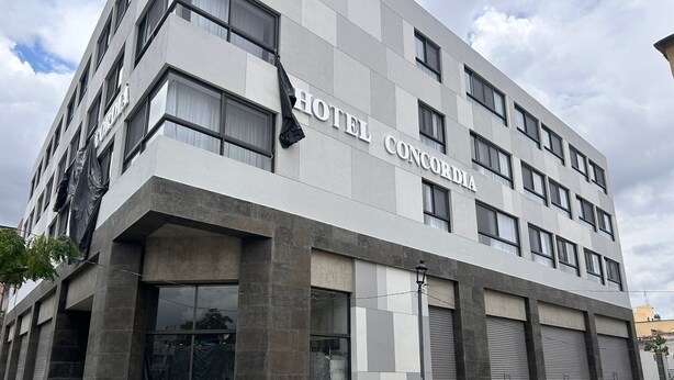 Un moderno edificio de hotel con el nombre "HOTEL CONCORDIA" en la fachada. Presenta un diseño simétrico con numerosas ventanas y balcones.