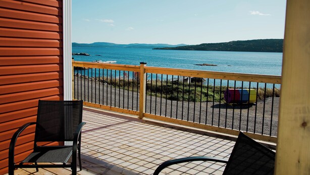 Un balcon donnant sur un lac et des montagnes, avec une balustrade en bois et une chaise.