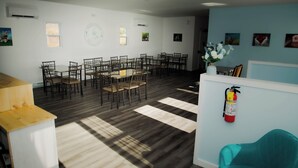 Une pièce spacieuse avec une grande table à manger entourée de chaises, un extincteur fixé au mur et un fauteuil turquoise dans un coin.