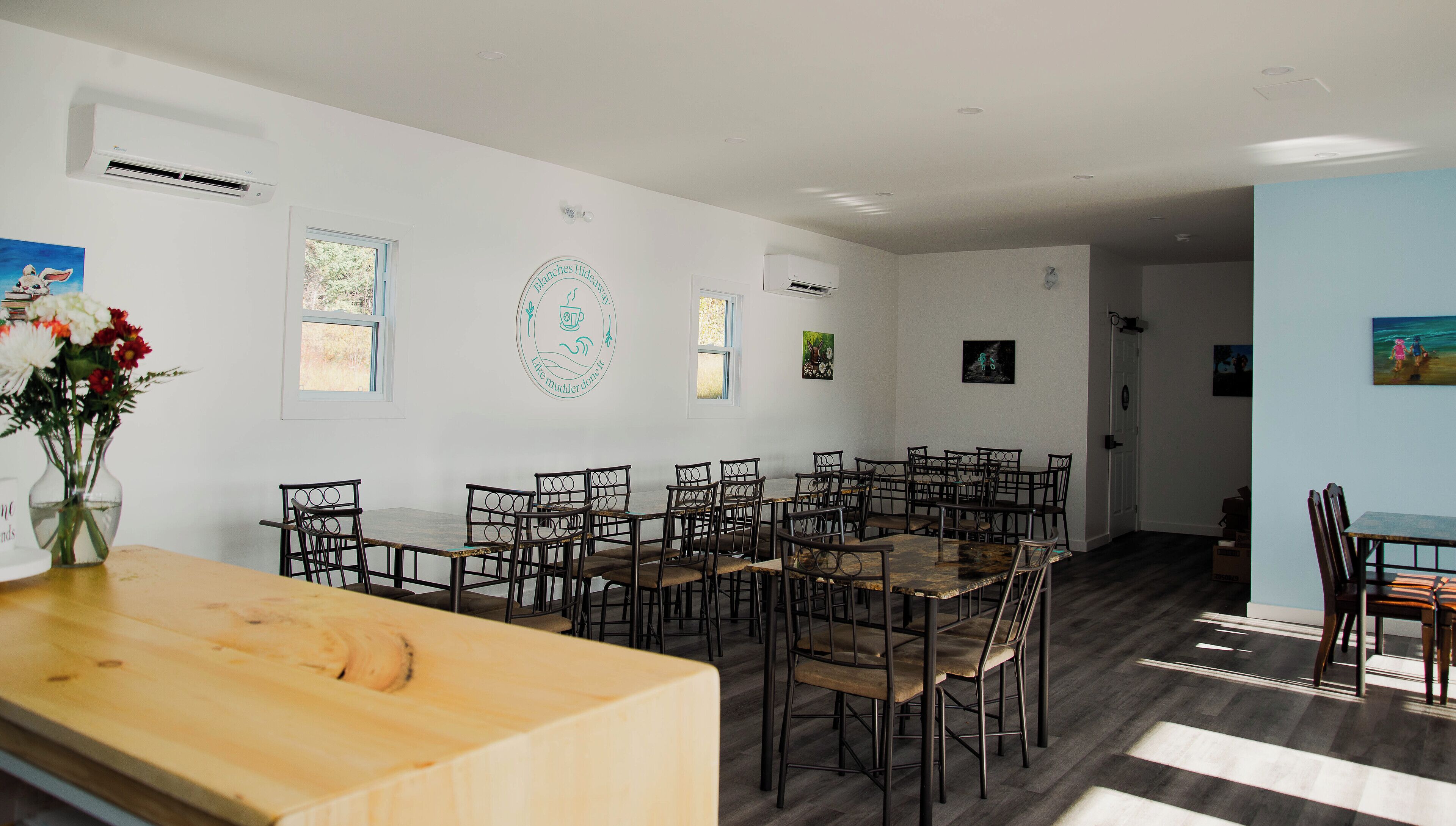 A dining area with multiple tables and chairs, a wooden counter, and artwork on the walls.