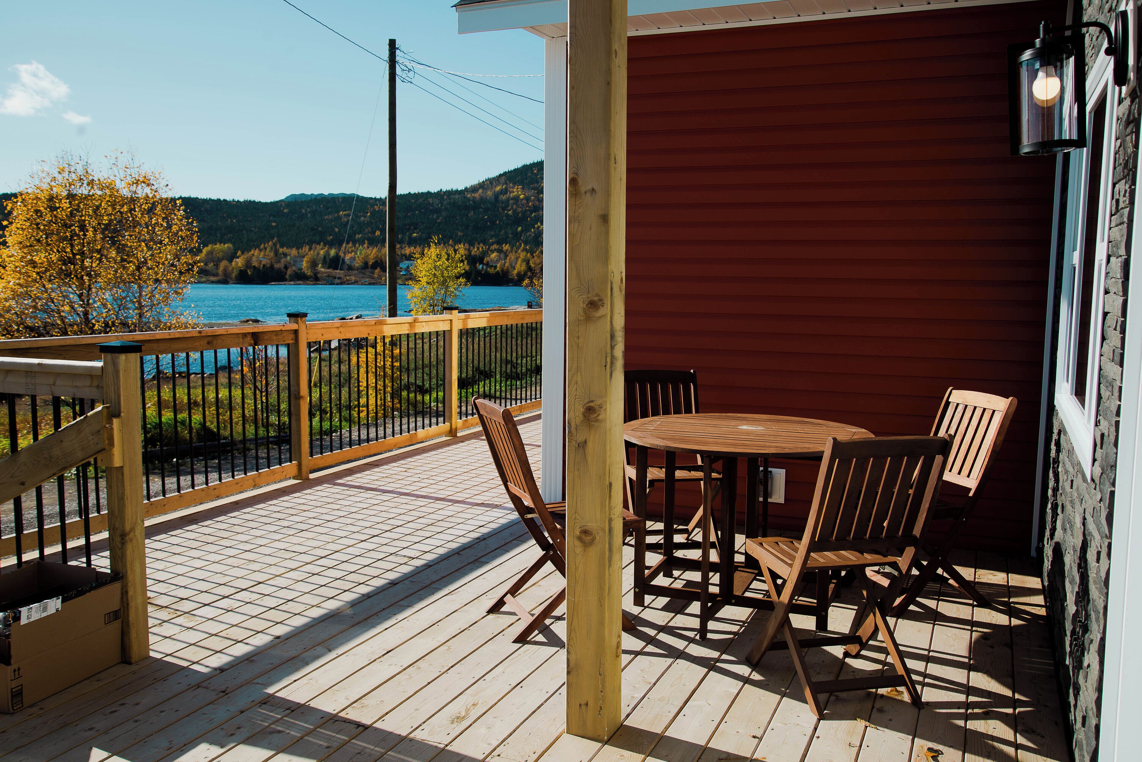 Um deck de madeira com mesa e cadeiras, com vista para um corpo de água e colinas.