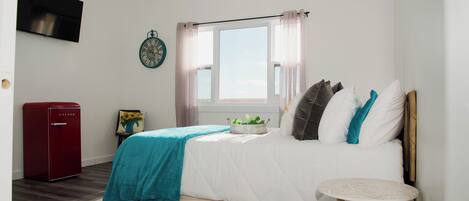 Ein Schlafzimmer mit einem Bett, einem kleinen Tisch, einem roten Gerät, einer Uhr und einem Fenster mit Vorhängen.