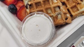 Un plateau avec des gaufres, des fraises, des myrtilles et un petit pot de crème fouettée.