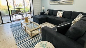 Un salon moderne avec un canapé d’angle, une table basse et un pouf rond.