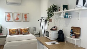 Quarto moderno com cama, mesa de cabeceira e um pequeno espaço de trabalho com micro-ondas e chaleira.