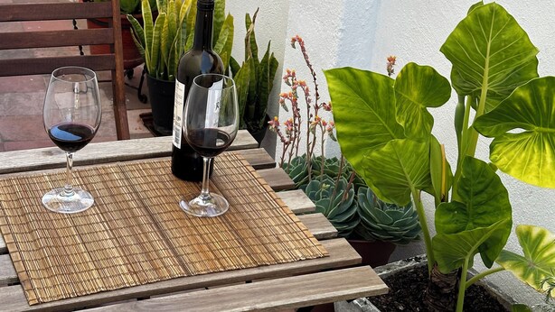 Um pátio com uma mesa posta para dois, com uma garrafa de vinho e dois copos.