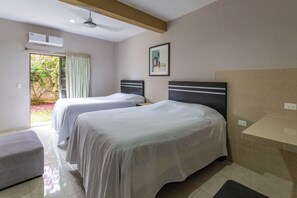 A hotel room with two beds, a bench, a ceiling fan, an air conditioning unit, a picture on the wall, and a view of the garden through the door. - Villa Bugambilias Near Bacalar Lagoon (Bacalar)