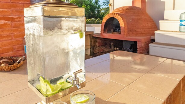 A bar area with a large ice dispenser and two glasses of a clear beverage, a brick oven, and a tiled counter. - Villa Bugambilias Near Bacalar Lagoon (Bacalar)