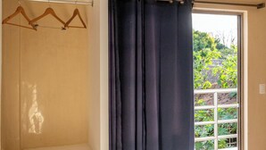 A room with a sliding glass door to a balcony, a white closet with wooden hangers, and a ceiling-mounted air conditioning unit. - Villa Bugambilias Near Bacalar Lagoon (Bacalar)