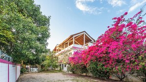 A two-story building with a wooden roof and a balcony, surrounded by lush greenery and vibrant pink bougainvillea flowers. - Villa Bugambilias Near Bacalar Lagoon (Bacalar)