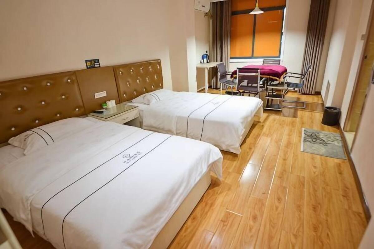 Hotellihuone, jossa on kaksi sänkyä, työpöytä, tuoli ja ikkuna, jossa on verhot.
