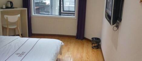 A hotel room with a bed, a desk, a chair, a television, and a window with curtains.