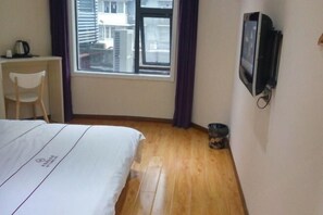 A hotel room with a bed, a desk, a chair, a television, and a window with curtains. - Huayi Business Hotel (Wuhan)