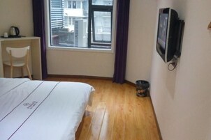 Habitación de hotel con cama, escritorio, silla, televisión y ventana con cortinas.