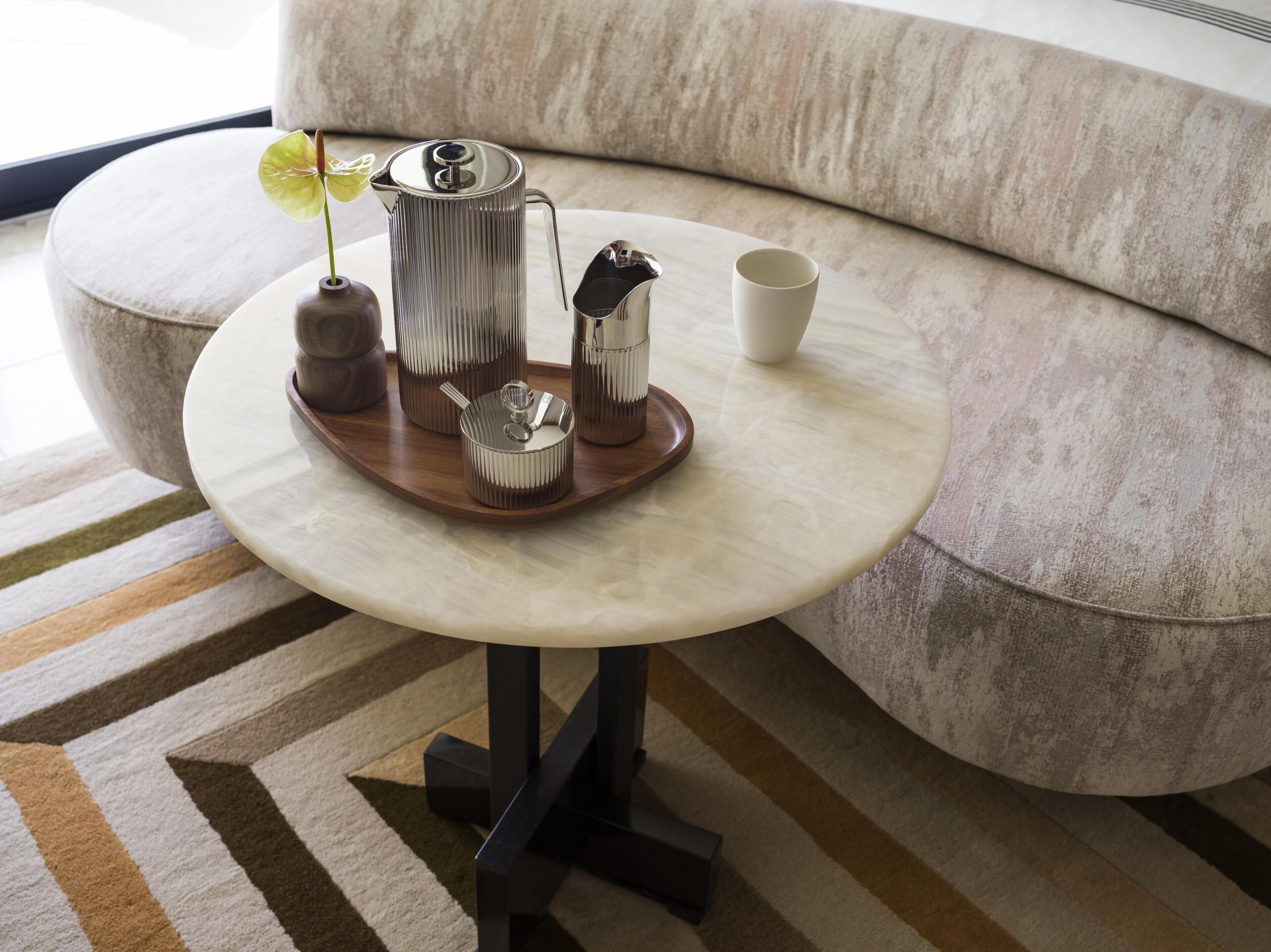 Een ronde tafel met een dienblad waarop een koffiezetapparaat, een kopje en een kleine schaal staan, geplaatst op een patroonrijk tapijt.