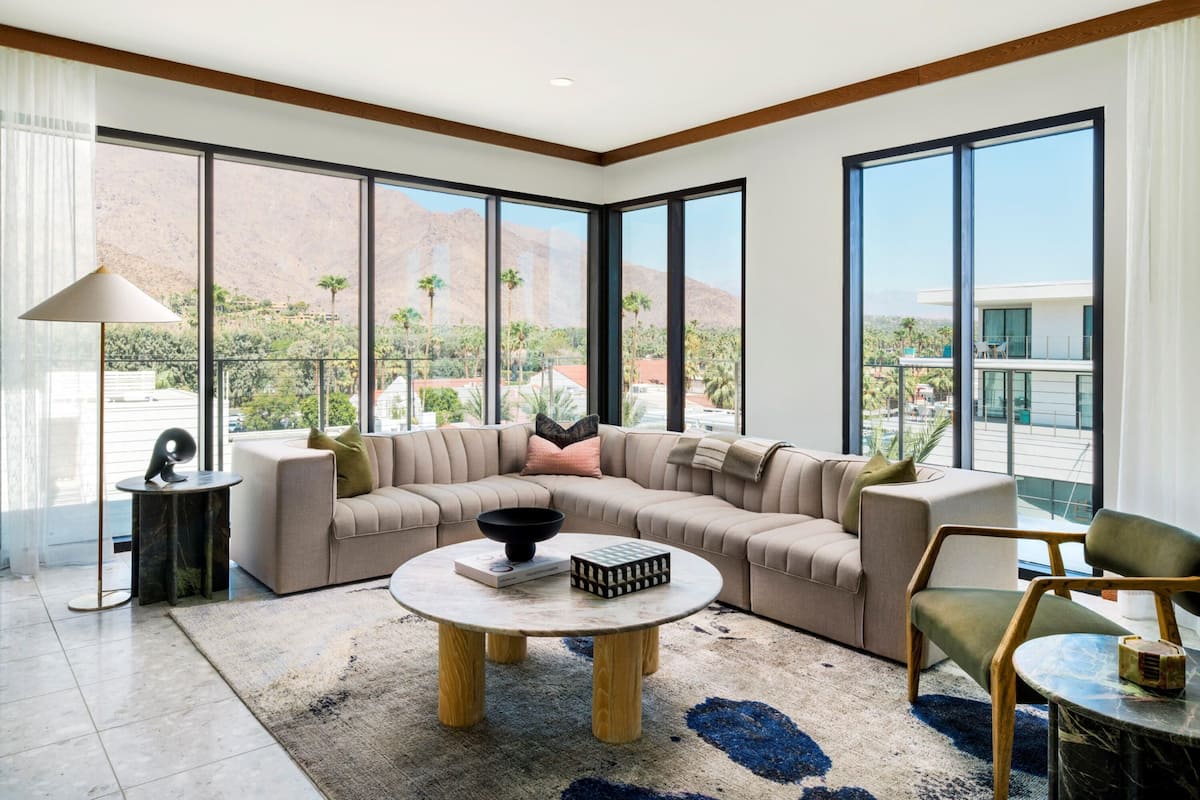 A modern living room with a sectional sofa, a round coffee table, and large windows offering a mountain view.