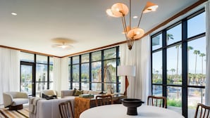 A modern living room with a sofa, chairs, a dining table, and large windows with a view of palm trees. - Thompson Palm Springs, by Hyatt (Palm Springs)