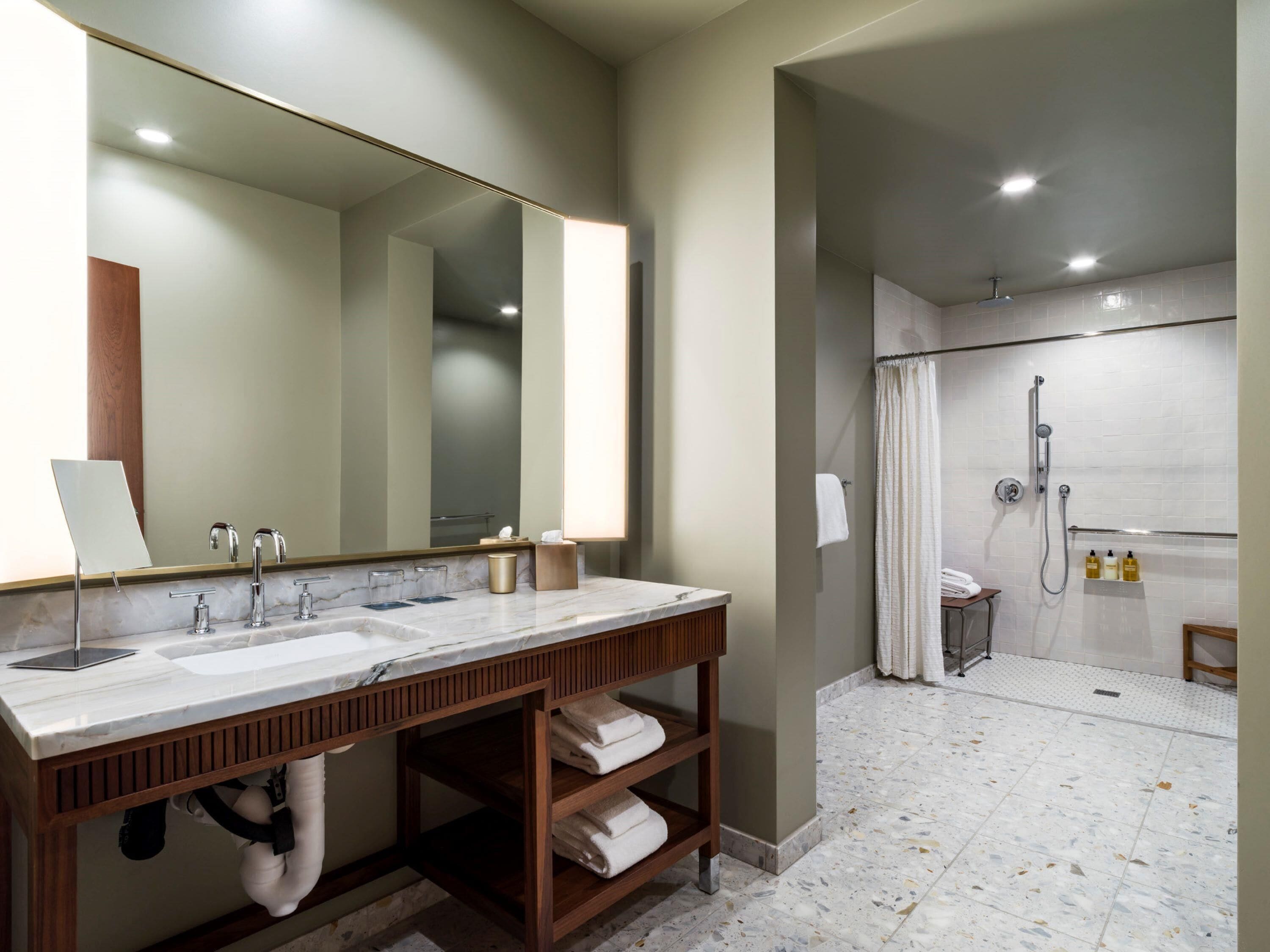 Une salle de bain avec un grand miroir, deux lavabos, une douche et un porte-serviettes.