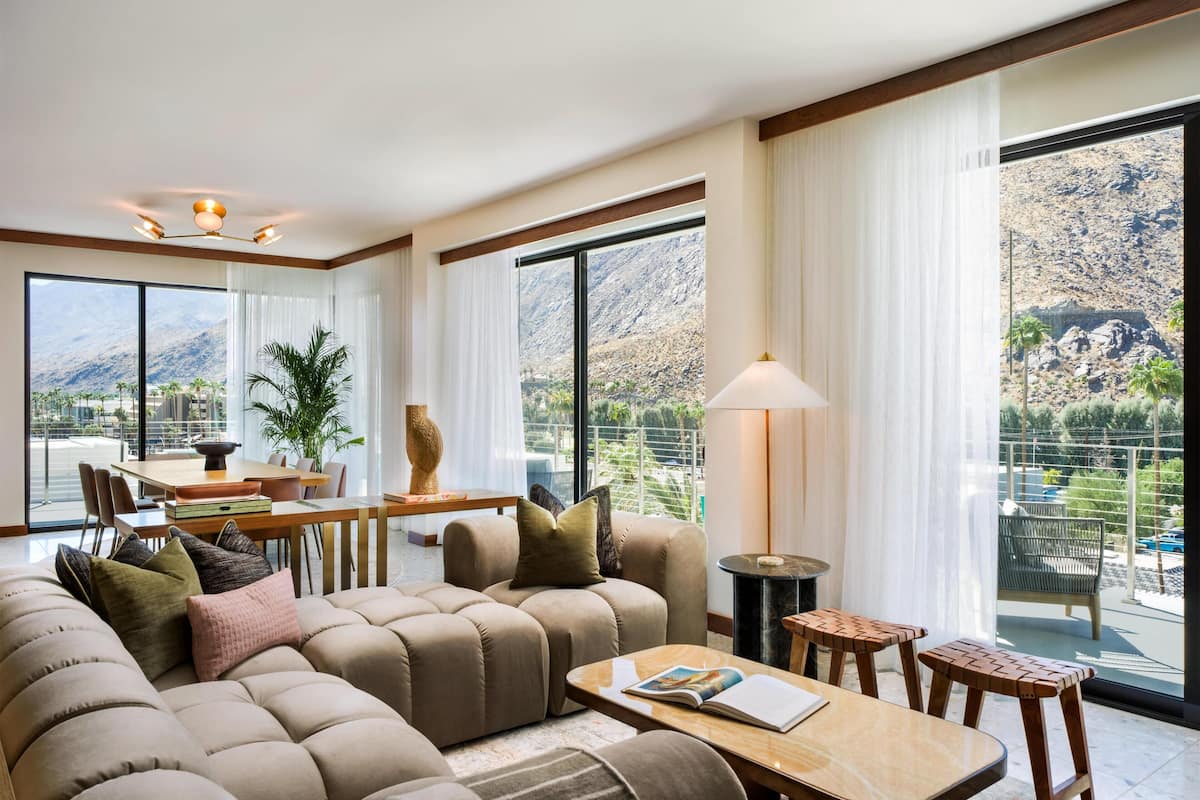 A modern living room with a large sofa, a dining table, and a view of mountains through large windows.