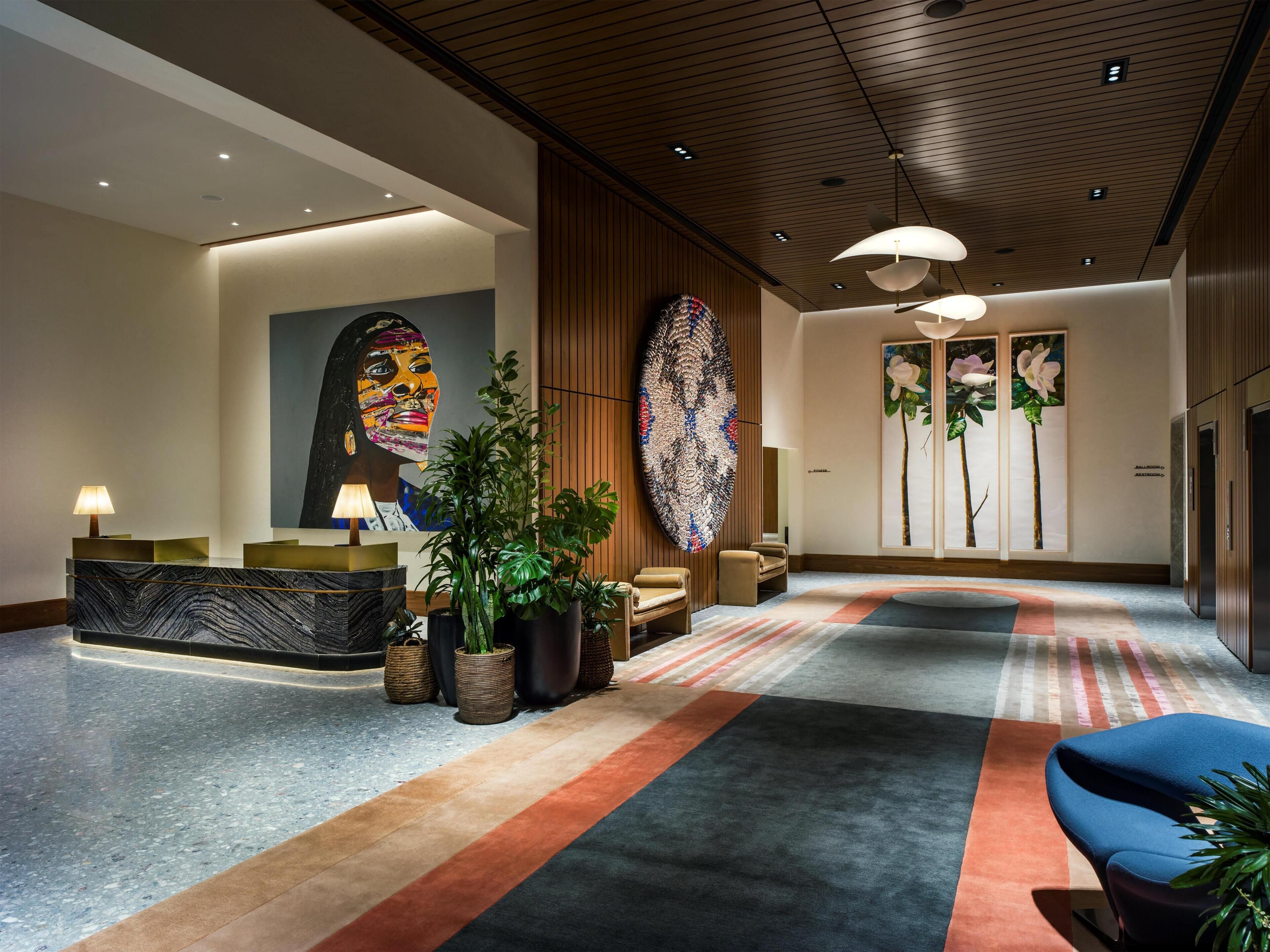 Un hall d’entrée moderne comprenant un comptoir d’accueil, un espace salon, de grandes œuvres d’art et une moquette à motifs.