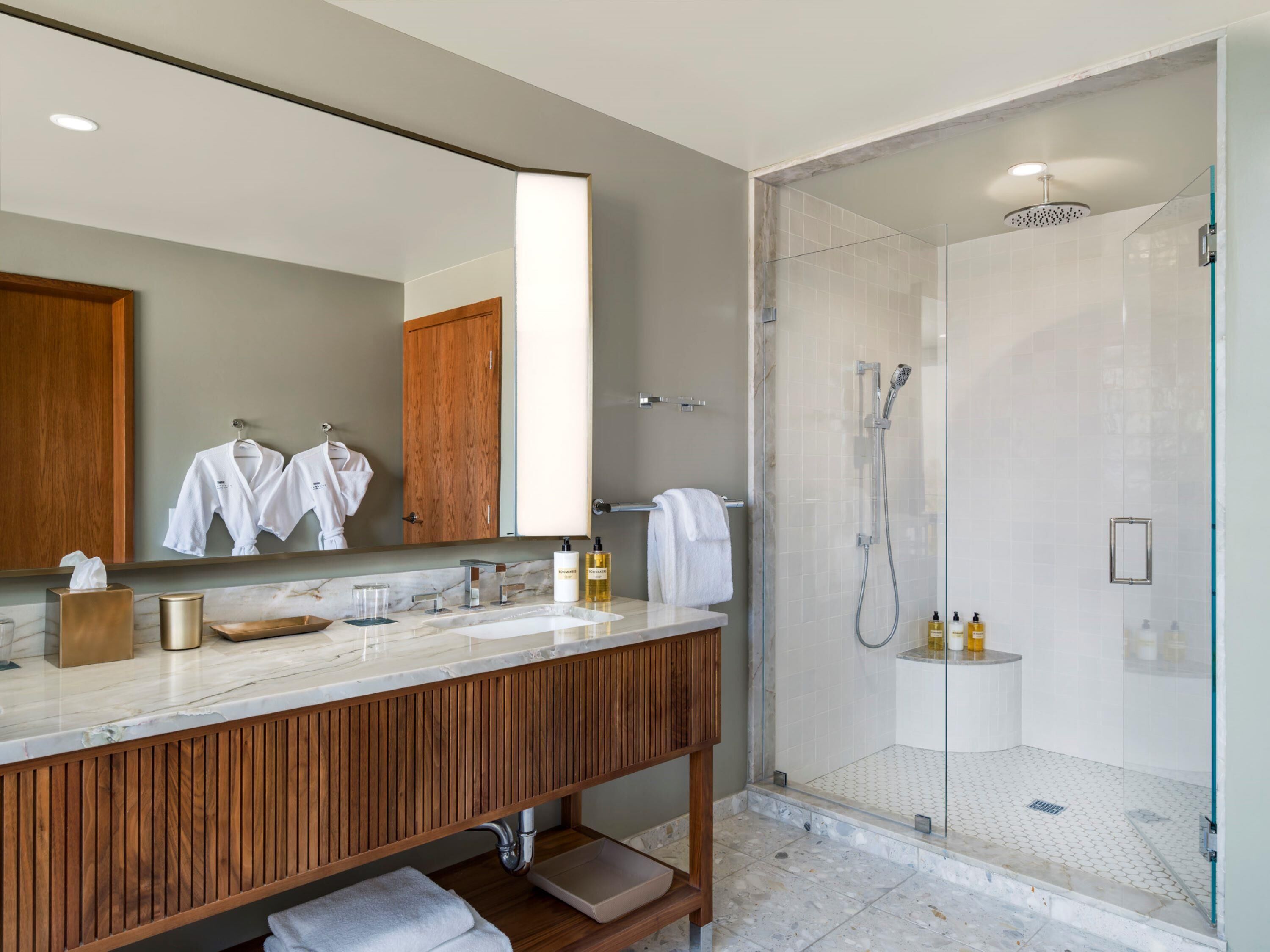 Une salle de bain moderne avec un meuble-lavabo en bois, un grand miroir, une douche à parois de verre et un comptoir en marbre.