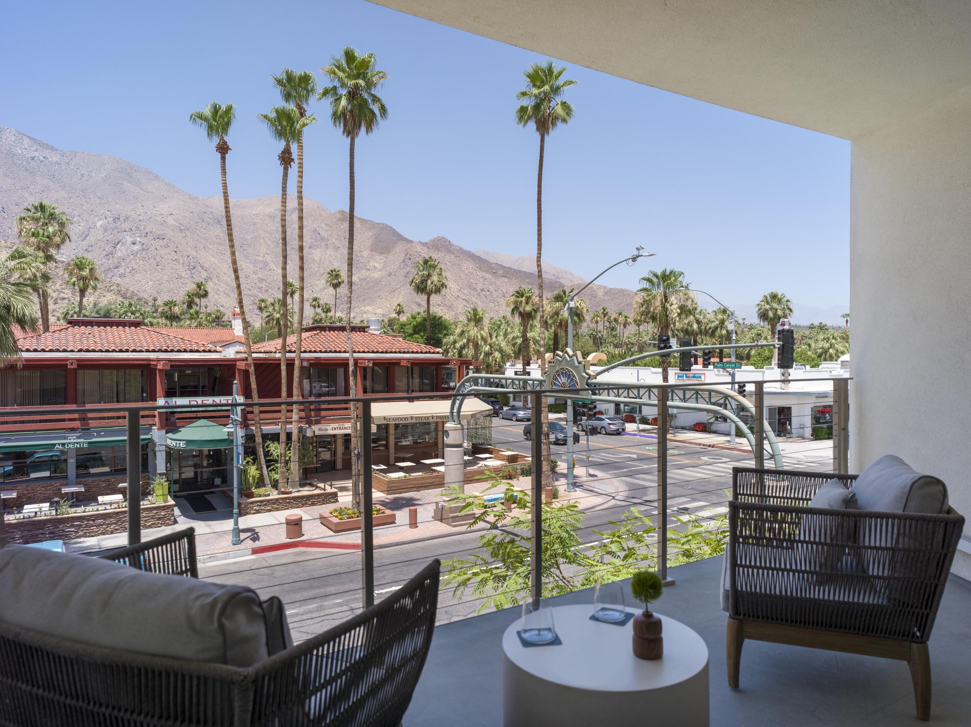 A balcony with wicker furniture, a view of a restaurant, and palm trees.