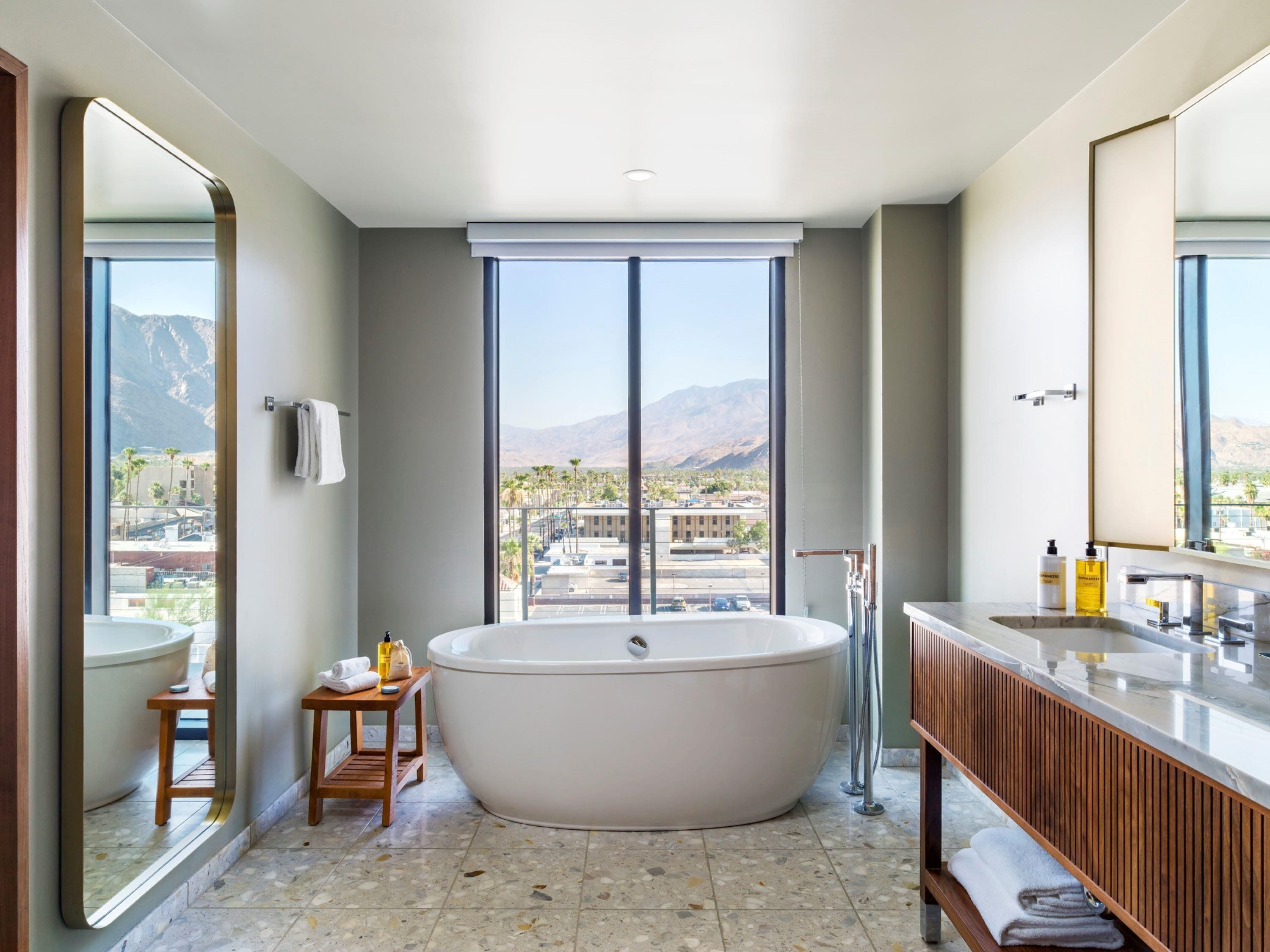 A modern bathroom with a freestanding bathtub, a large mirror, and a view of mountains through the window.