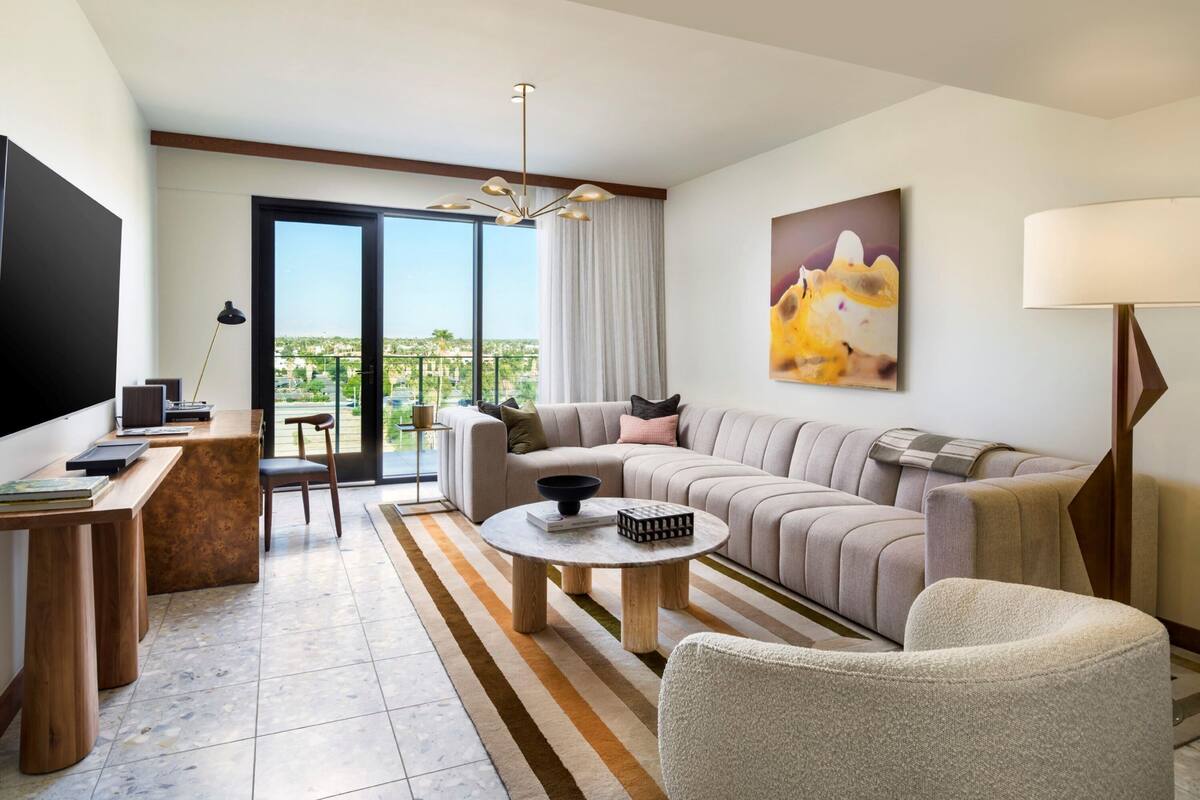 A modern living room with a sofa, coffee table, and a TV. There's a balcony with a view.