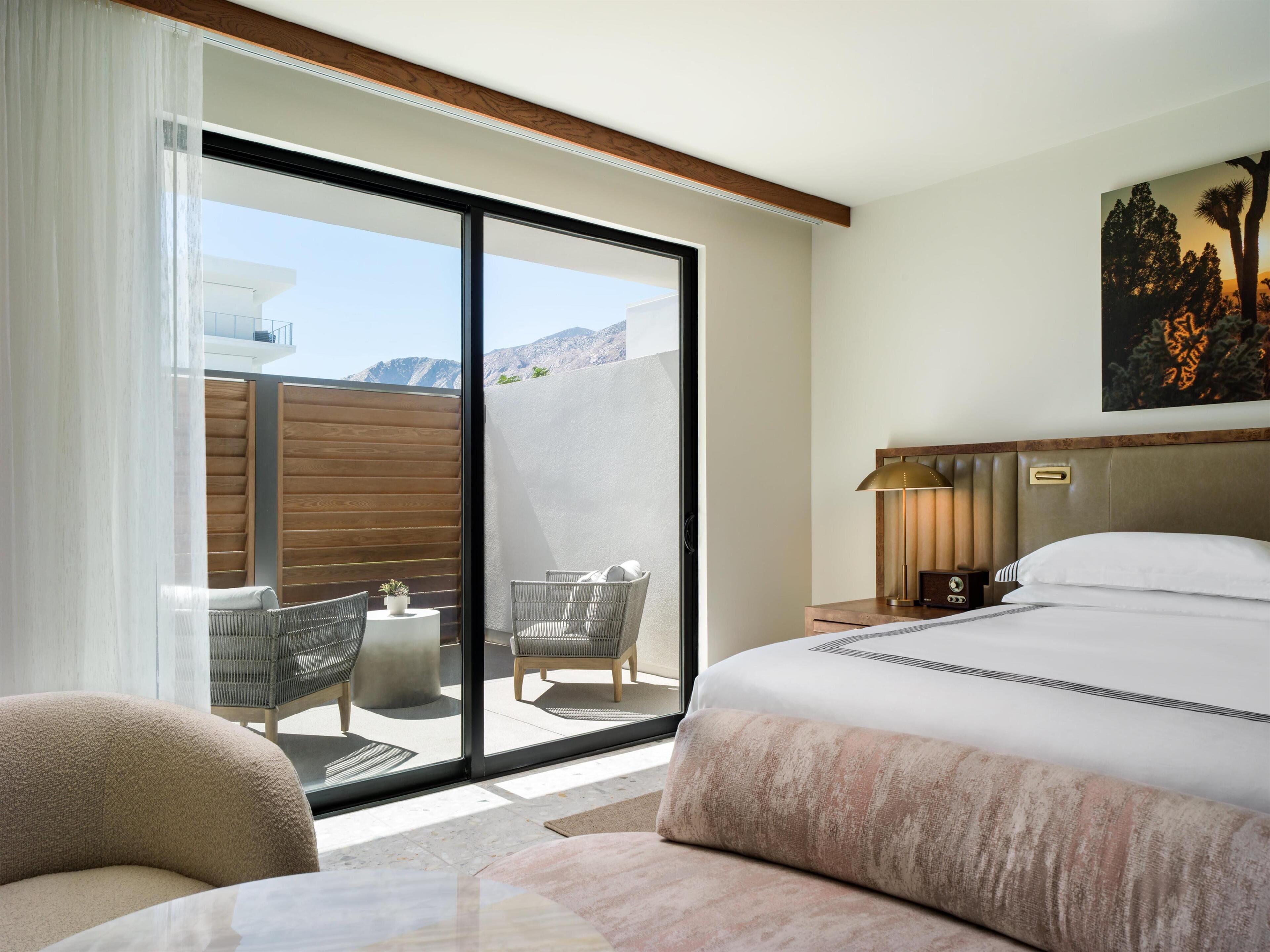 Ein Hotelzimmer mit einem großen Bett, einem Schreibtisch, einem Sessel, einer Couch, einem Balkon mit Sitzgelegenheiten und einem Bild an der Wand.