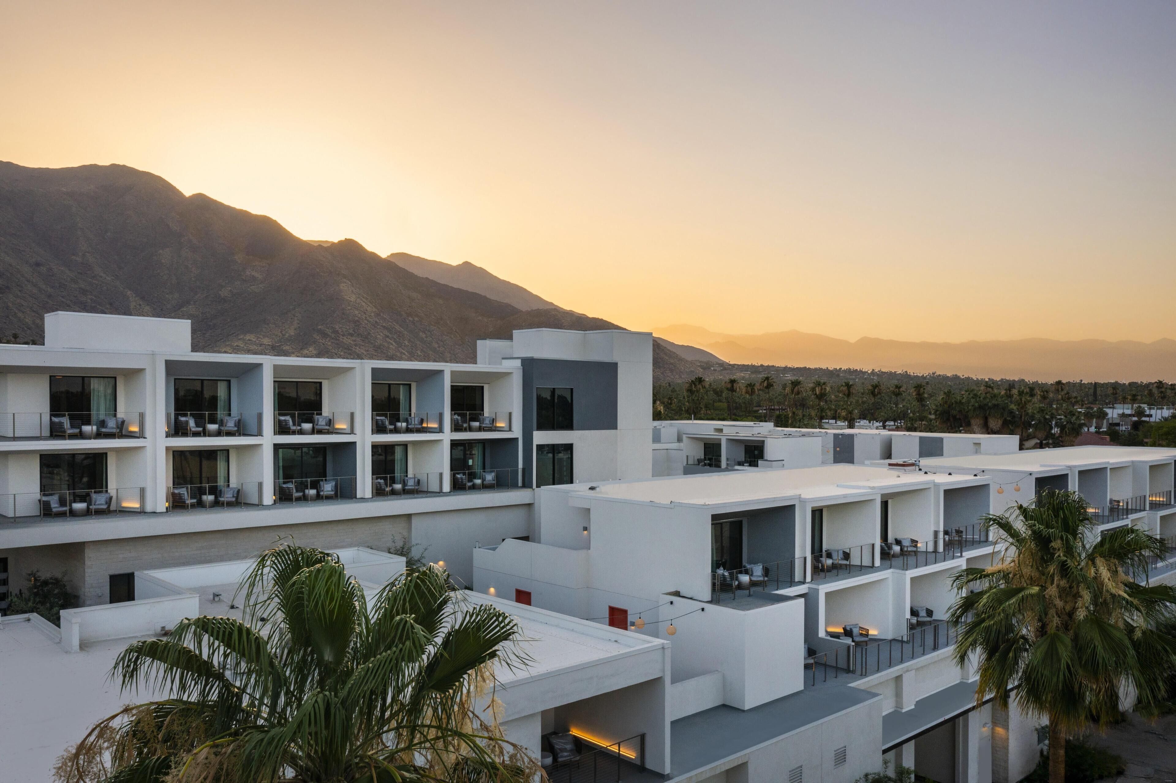 A modern hotel with multiple floors, balconies, and a view of mountains.