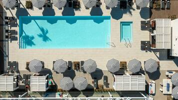 An aerial view of a hotel pool area with multiple lounge chairs and umbrellas, a large central pool, and a separate smaller pool.