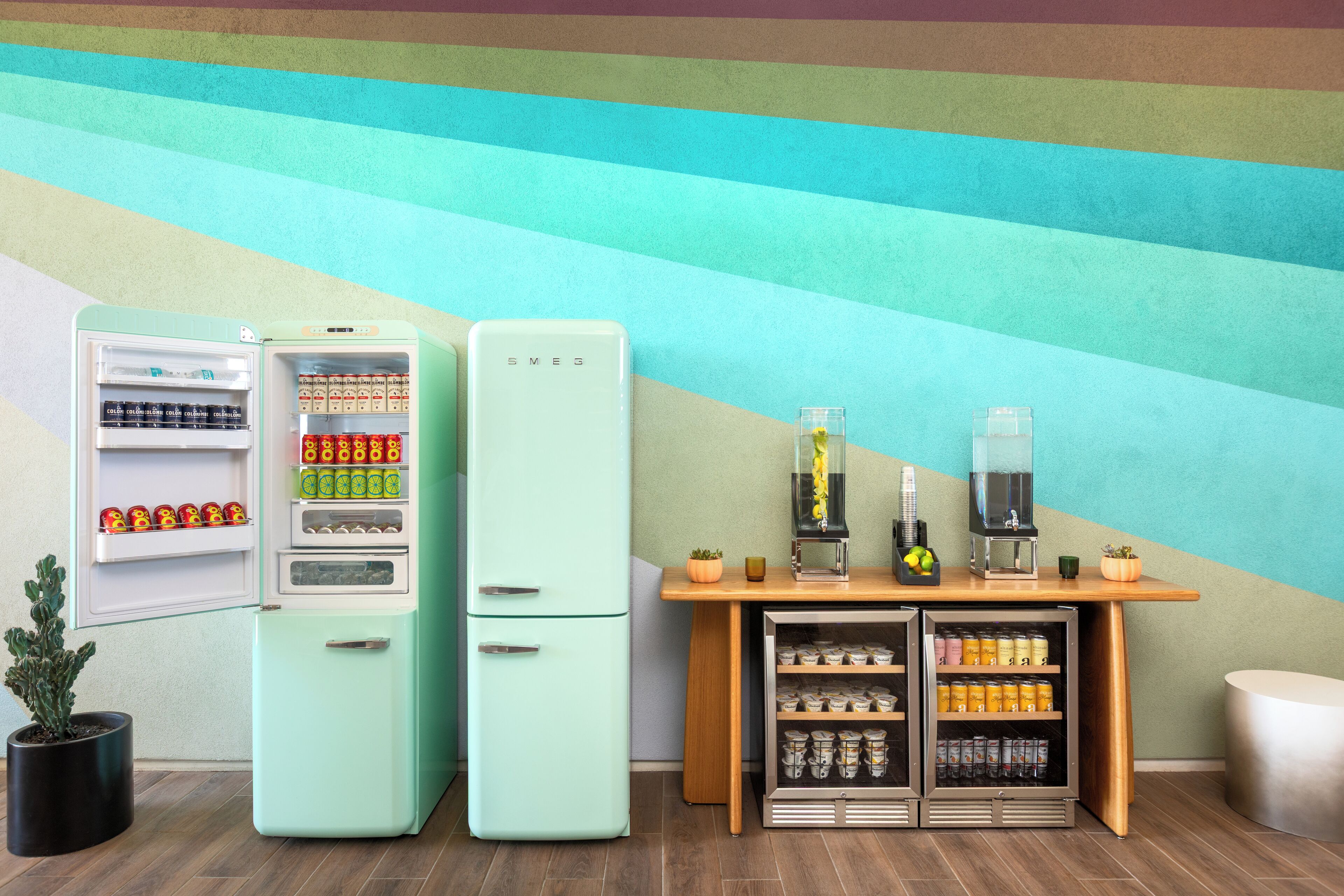 A room with two vintage-style refrigerators, a small wooden table with a coffee machine, and a potted plant.