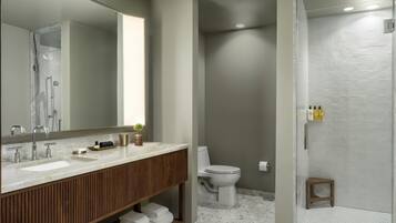 A modern bathroom with a large mirror, two sinks, a toilet, and a walk-in shower.
