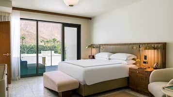 A hotel room with a bed, bedside table, lamp, and a view of a mountainous landscape through a sliding door.