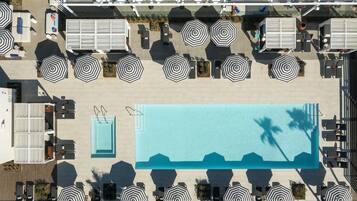 An aerial view of a rooftop pool area with multiple lounge chairs and umbrellas, a swimming pool, and a bar area.
