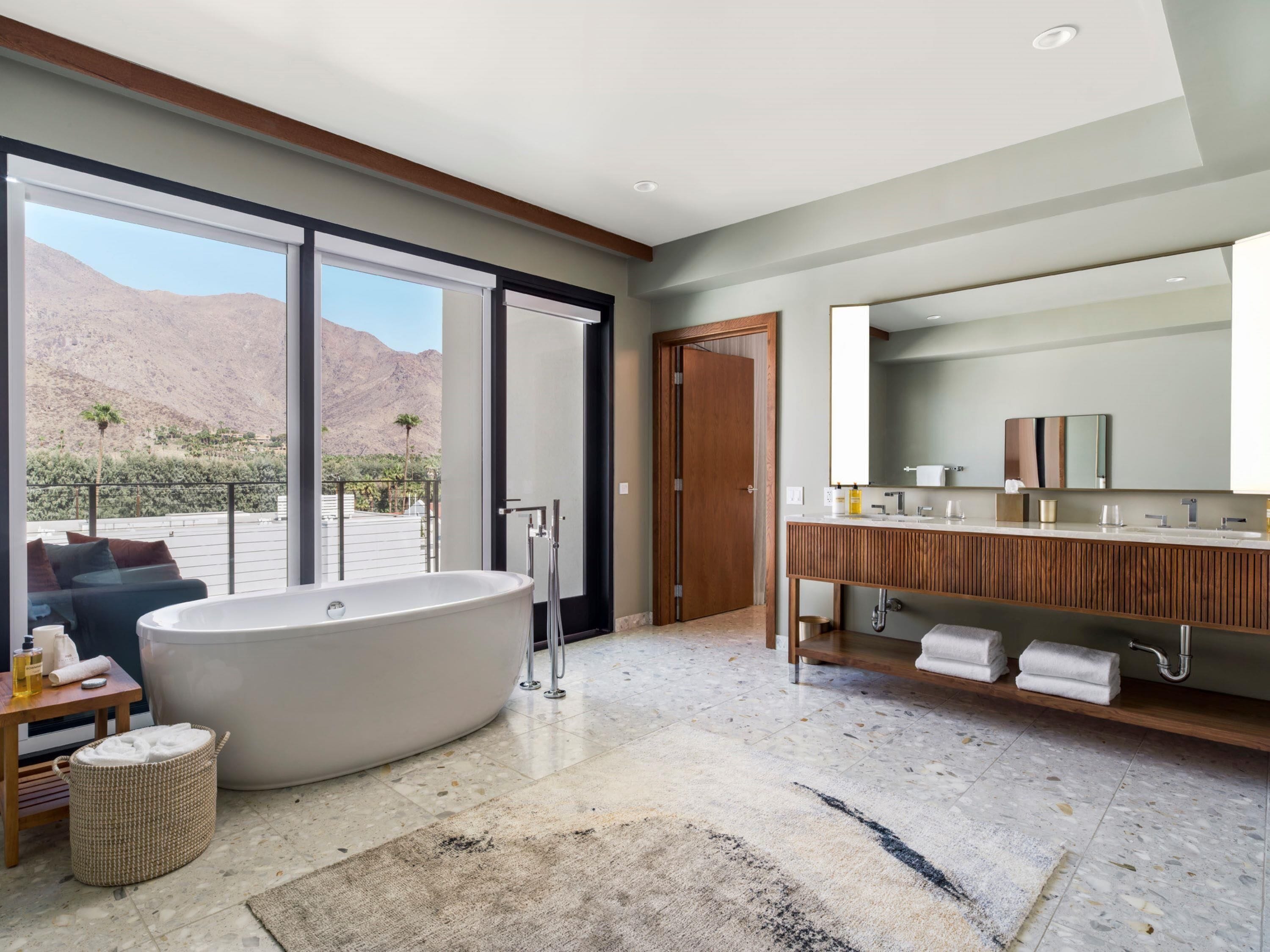 Un baño moderno con una bañera independiente, un tocador de madera y un espejo grande.