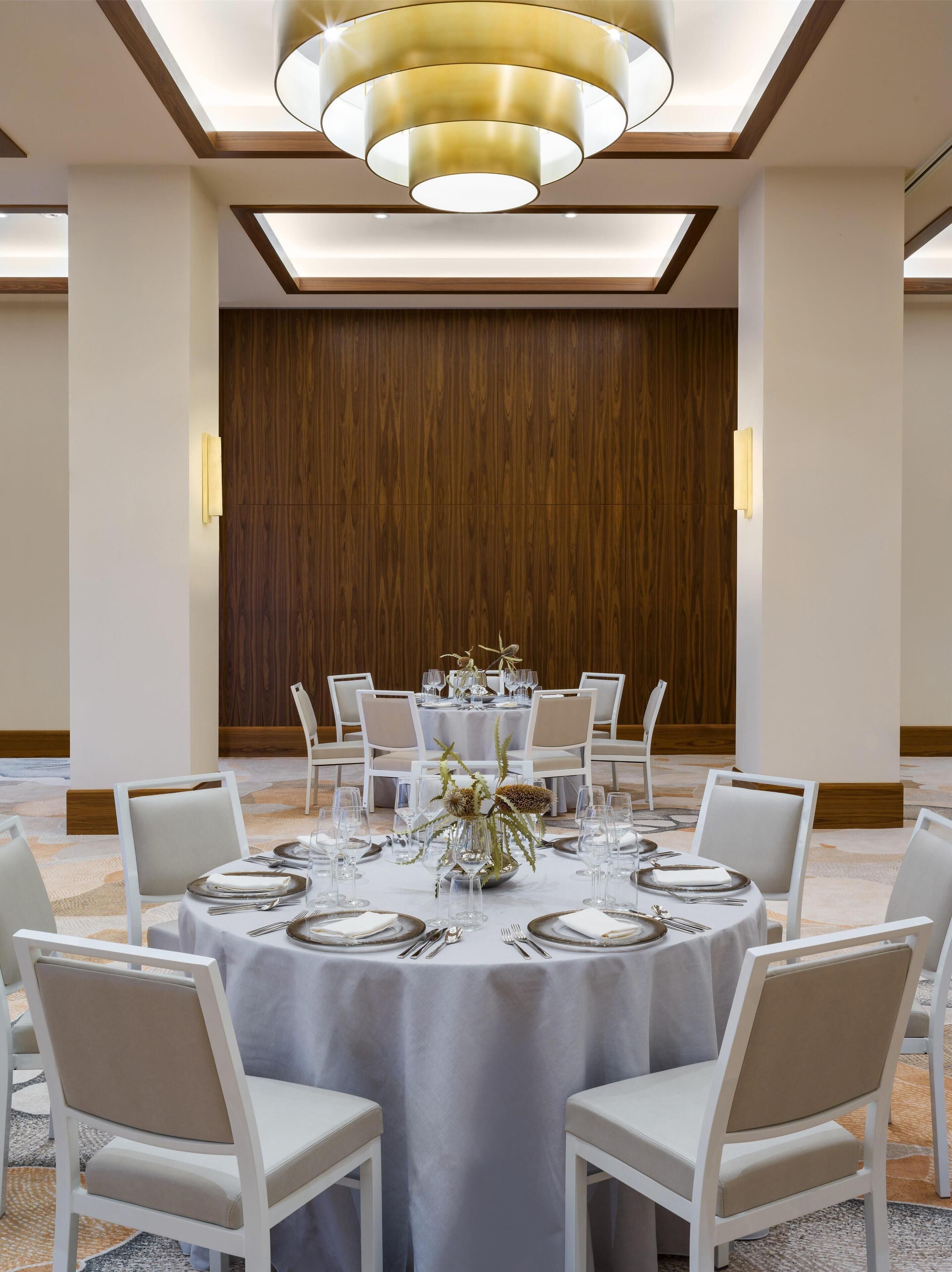 Une salle de conférence avec une table ronde, des chaises blanches et un lustre moderne.