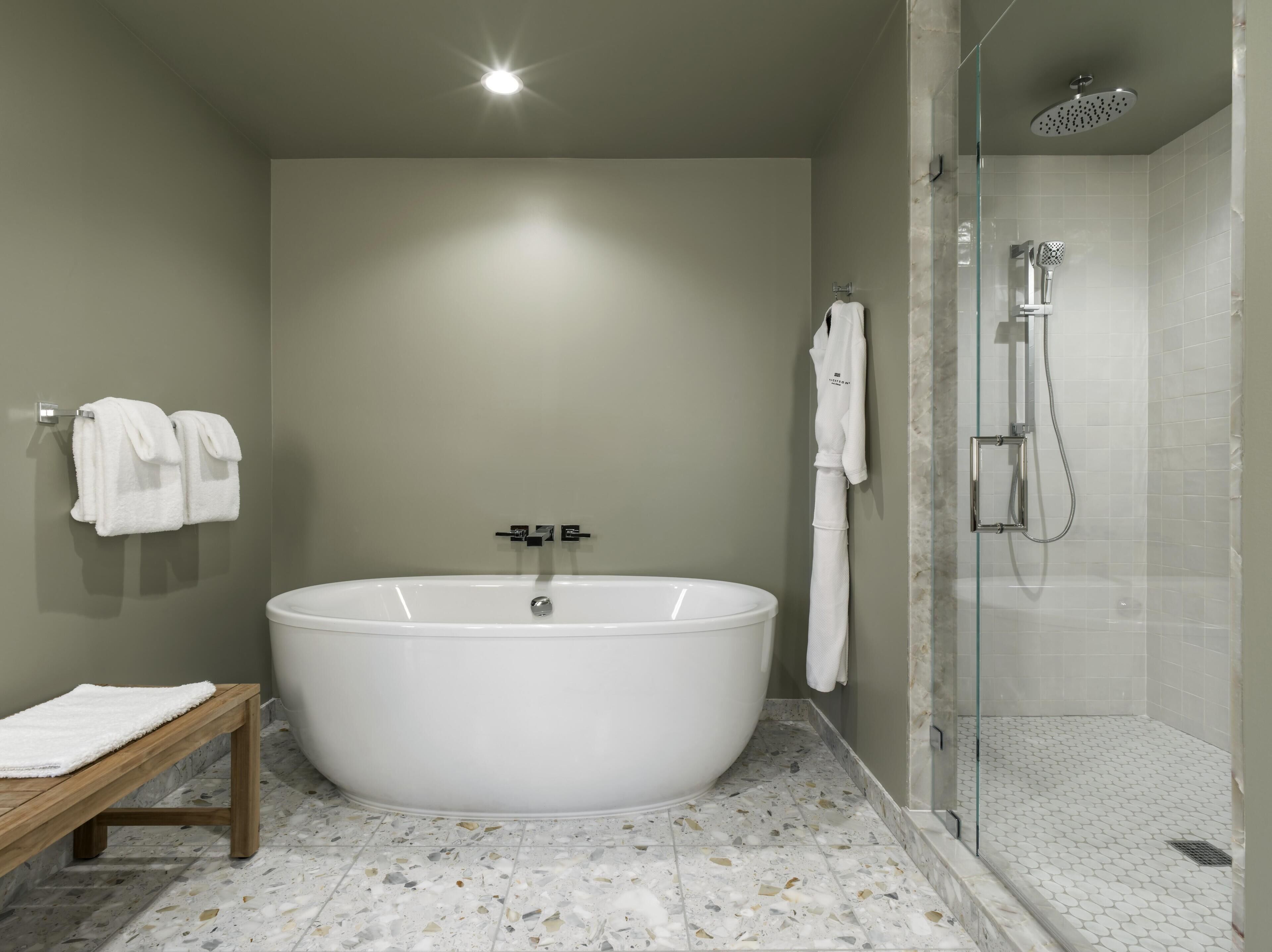 A modern bathroom with a freestanding bathtub, a glass shower enclosure, and a bench with towels.