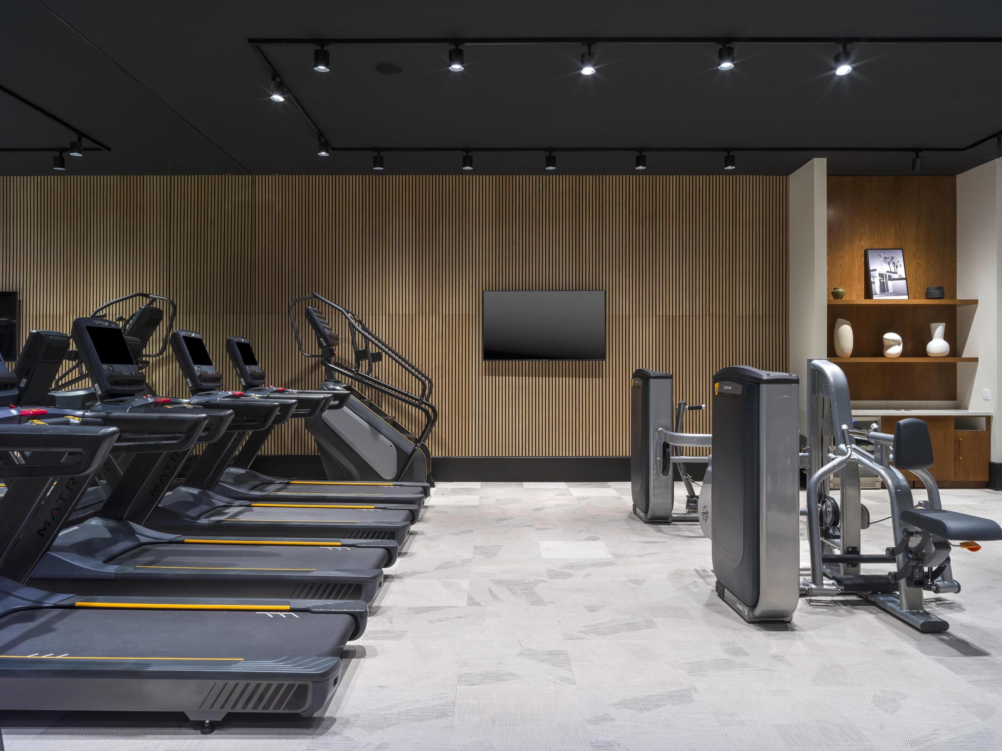 Un gimnasio con cintas de correr, máquinas de pesas y un televisor en la pared.