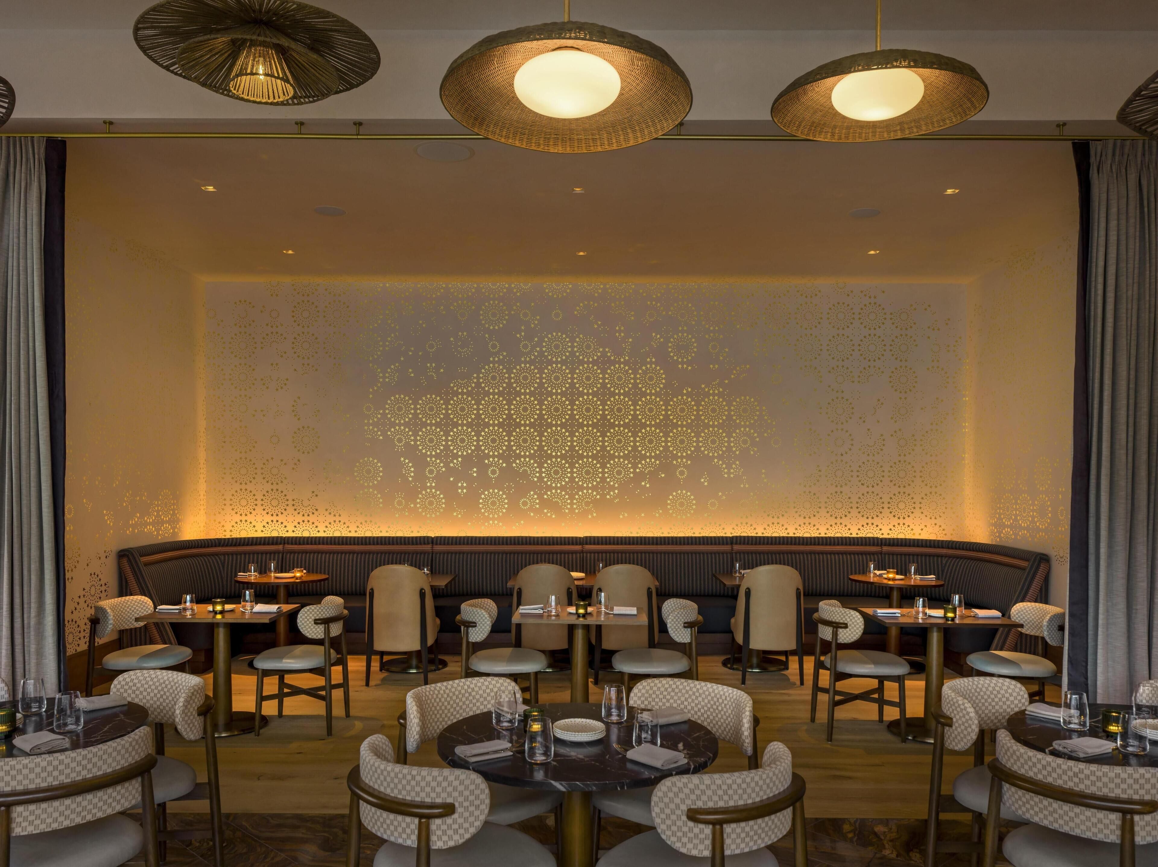 A restaurant with round tables, cushioned chairs, and decorative ceiling lights.